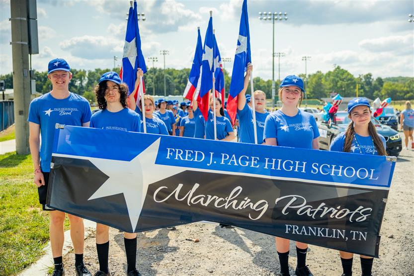 Marching band members stand behind a banner